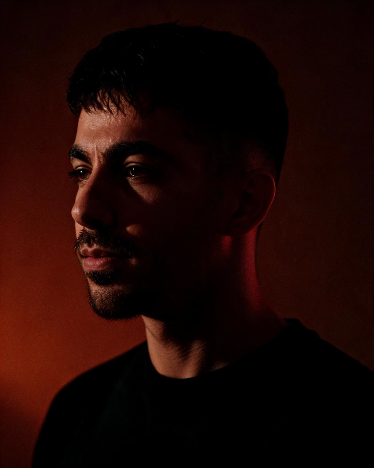 Iman Benjamin, photographed in profile against a dark red backdrop.