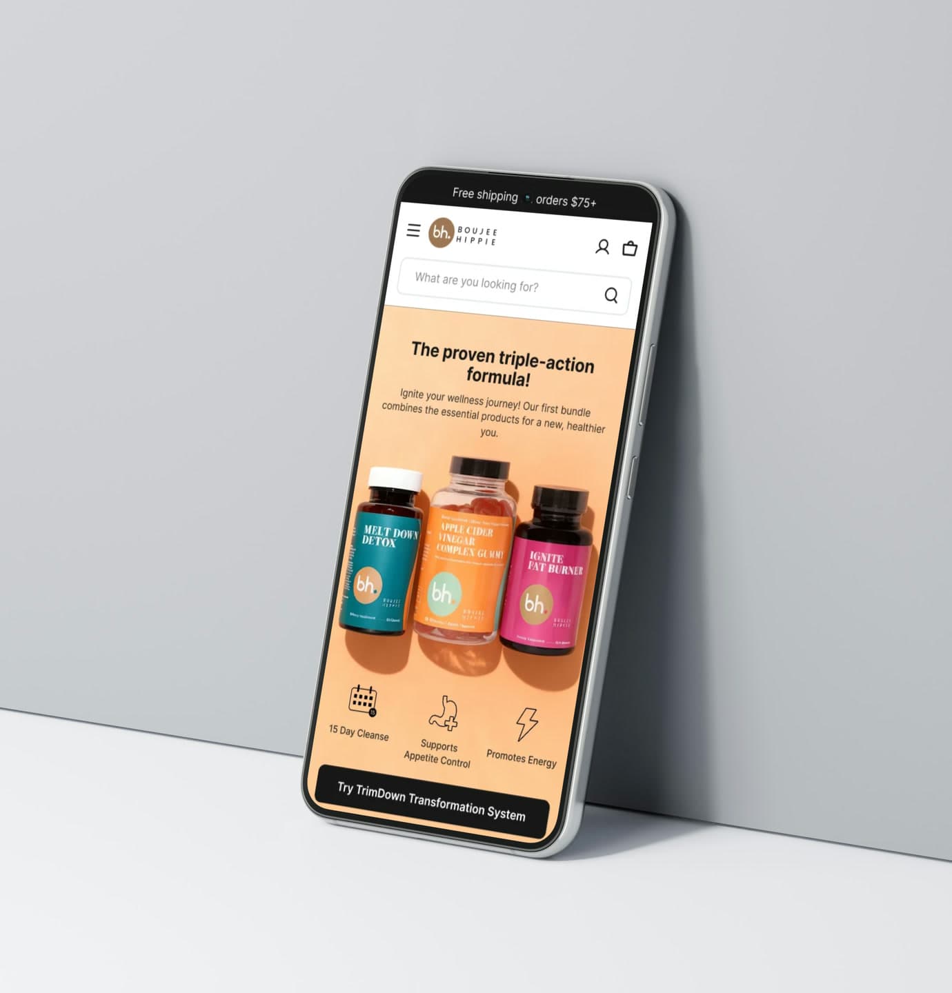 The Boujee Hippie supplement bundle page on a phone propped against a pale grey wall, showing three labelled bottles side by side on a peach background.