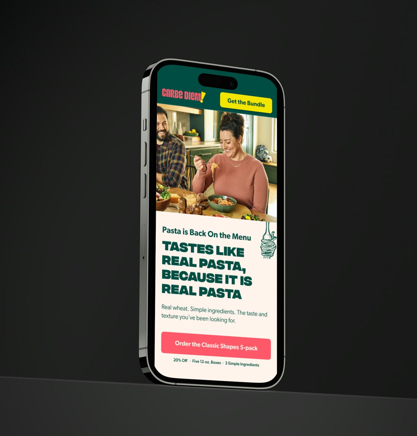 The Carbe Diem landing page on a phone angled against a black backdrop, showing a couple eating pasta in a kitchen above the headline “Tastes like real pasta, because it is real pasta”.